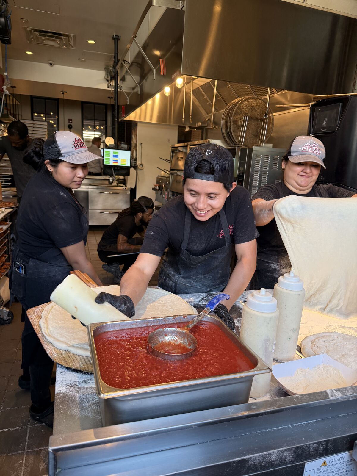 The Andy's Pizza kitchen crew making pizza — sauce, dough, and smiles